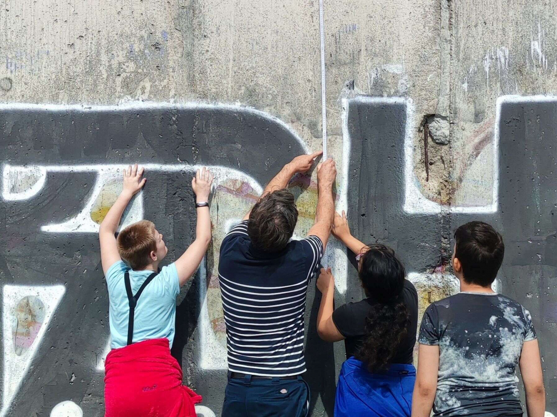 Jugendgruppe misst Höhe der Mauer mit einem Zollstock